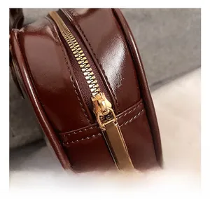 Detailed close-up of golden zipper hardware on a dark brown glossy faux leather handbag