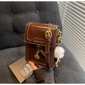 Detail of dark brown leather crossbody phone bag with gold buckle and fuzzy charm