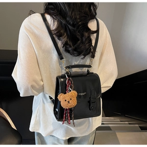 Detailansicht eines schwarzen PU-Lederrucksacks mit Silberschnalle und Bärenanhänger an Model