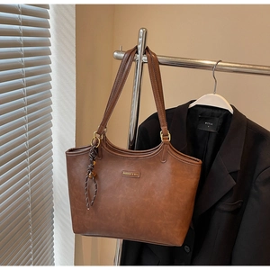 Detail einer braunen Leder-Shopper-Tasche mit Metall-Logo und Knotanhänger an einem Verkaufsständer