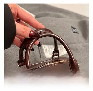 Detail of round handles and gold hardware on a glossy brown oil leather satchel bag