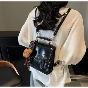 Detail eines schwarzen glänzenden Mini-Rucksacks mit Doppelriemen und Bärenanhänger