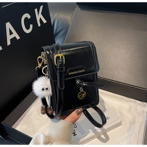 Detail of black faux leather phone bag with gold lettering and white pompom charm