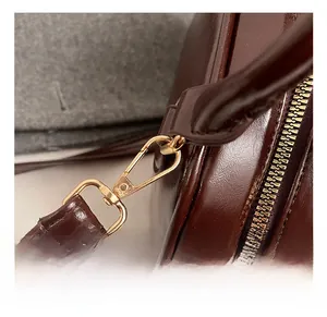 Macro view of gold metal swivel hook and oil wax leather texture on brown crossbody bag