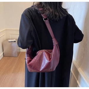 Detailed view of a burgundy leather crescent bag styled with a minimalist black coat