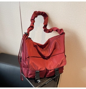 Detail of burgundy nylon tote bag with pleated straps and functional buckle pockets