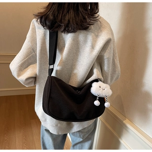Detailansicht der schwarzen Cord-Tasche mit weißem Plüsch-Anhänger und breitem Schultergurt