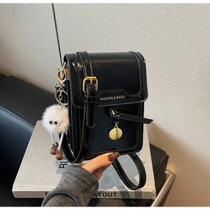 Detail of black PU leather crossbody phone bag with gold lettering and plush monster charm
