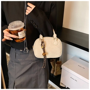 Detail of a creamy beige crossbody bag with textured finish and decorative knotted charm