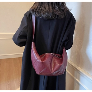 Deep burgundy moon-shaped crossbody bag with glossy oil-wax texture on a female model