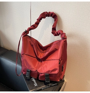 Detail of burgundy nylon tote bag featuring scrunchie straps and dual buckle pockets