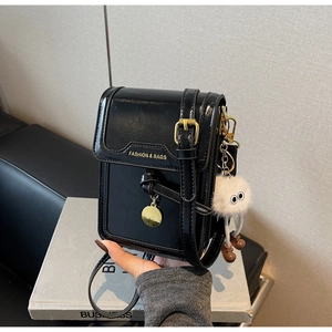 Detail of black patent leather crossbody bag with gold hardware and plush monster charm