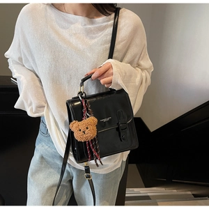 Detail der schwarzen glänzenden Ledertasche mit Metallschnalle und Teddybär-Anhänger