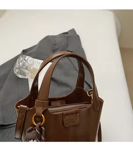 Close-up of brown oiled leather bucket bag with embossed logo and plush bear charm