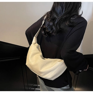 Detail of a creamy white half-moon bag with pleated faux leather texture on a shoulder strap