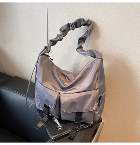 Detail of grey nylon tote bag showing wide pleated strap and front utility buckle pockets