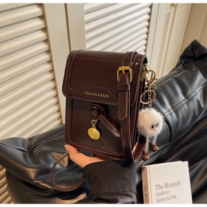 Detail view of dark brown glossy crossbody bag with metal buckle and plush monster charm