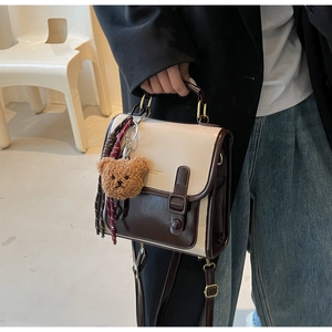 Detail der Retro-Handtasche mit poliertem Metallgriff und süßem Bären-Anhänger