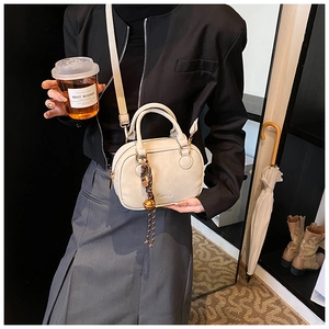Detail of a creamy white mini Boston bag with gold bell charm and shoulder strap