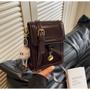 Detail of dark brown vintage mobile phone bag with plush charm and gold hardware