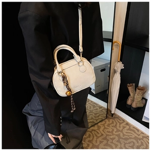 Detail of a beige crossbody bag with metal chain pendant and a small gold bell