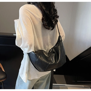 Detail of black pleated patent leather crescent bag worn as a shoulder bag on a model