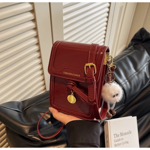Close-up of burgundy crossbody phone bag with gold charm and white plush toy detail