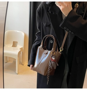 Detail of a brown glossy bucket bag with a cute bear charm and a detachable strap