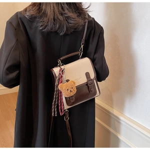 Details der zweifarbigen Vintage-Umhängetasche mit Schnallen und Plüschbär-Anhänger