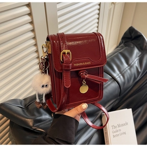 Close-up of deep red glossy leather crossbody bag with cute pom-pom monster pendant