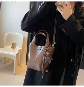 Brown bucket bag in glossy oil wax leather with a cute bear charm and woven strap