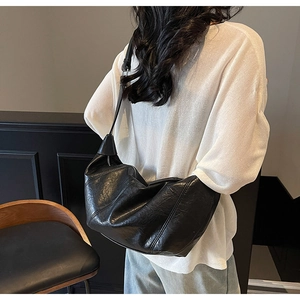 Detail of black leather dumpling bag featuring textured pleats and soft shoulder strap