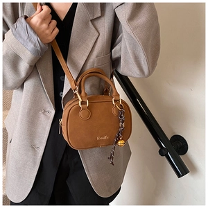 Brown retro small crossbody bag with matte texture and decorative bell charm on a model
