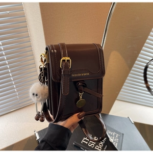 Detail of dark brown leather mini flap bag with plush charm and fashion text