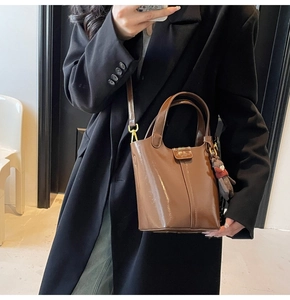 Close-up of brown shiny leather bucket bag with gold hardware and plush bear charm