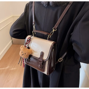 Detail der Vintage-Umhängetasche mit weißer Klappe und süßem Bärenanhänger-Dekor
