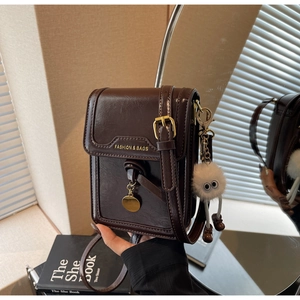 Detail of vintage brown textured crossbody bag with plush monster charm and gold pendant