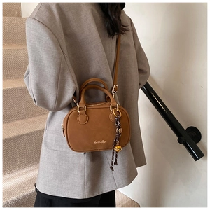 Detail of a brown vintage crossbody bag with woven pendant on grey blazer