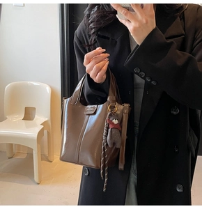 Close-up of a dark brown glossy leather bucket bag with a plush bear charm and tassel