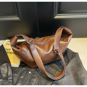 Detail of dark brown leather crescent bag with textured finish and silver zipper closure