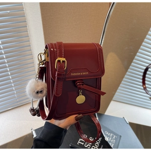 Detail of dark red glossy leather phone bag with gold buckle and plush pendant charm