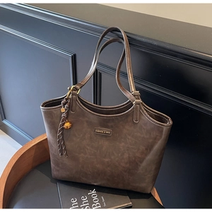 Detail einer dunkelbraunen Leder-Shopper mit Mode-Tag und Quaste auf schwarzem Stuhl