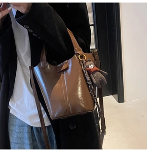 Detail of dark brown patent leather bucket bag with bear charm and silk scarf handle