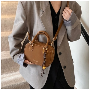 Detail of a brown suede crossbody bag with gold hardware and tassel charm on a model