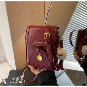 Detail of red leather crossbody phone bag with embossed text and a plush charm