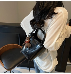 Close-up of black glossy bucket bag with handle and cute brown bear pendant detail