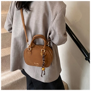 Close-up of brown Boston handbag with gold Ximeto logo and woven decorative pendant