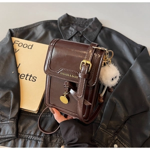 Detail of dark brown leather phone bag with magnetic flap and cute plush ball charm