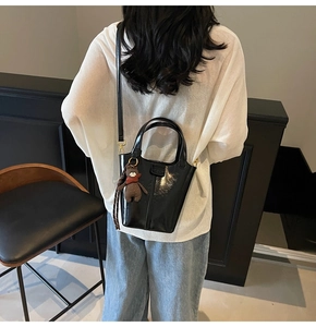 Detail of a black shiny bucket bag with brown teddy bear charm worn by a model