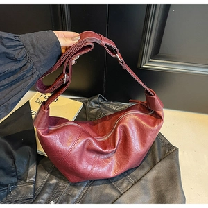 Detail of burgundy crescent bag in premium textured leather being held over a black jacket